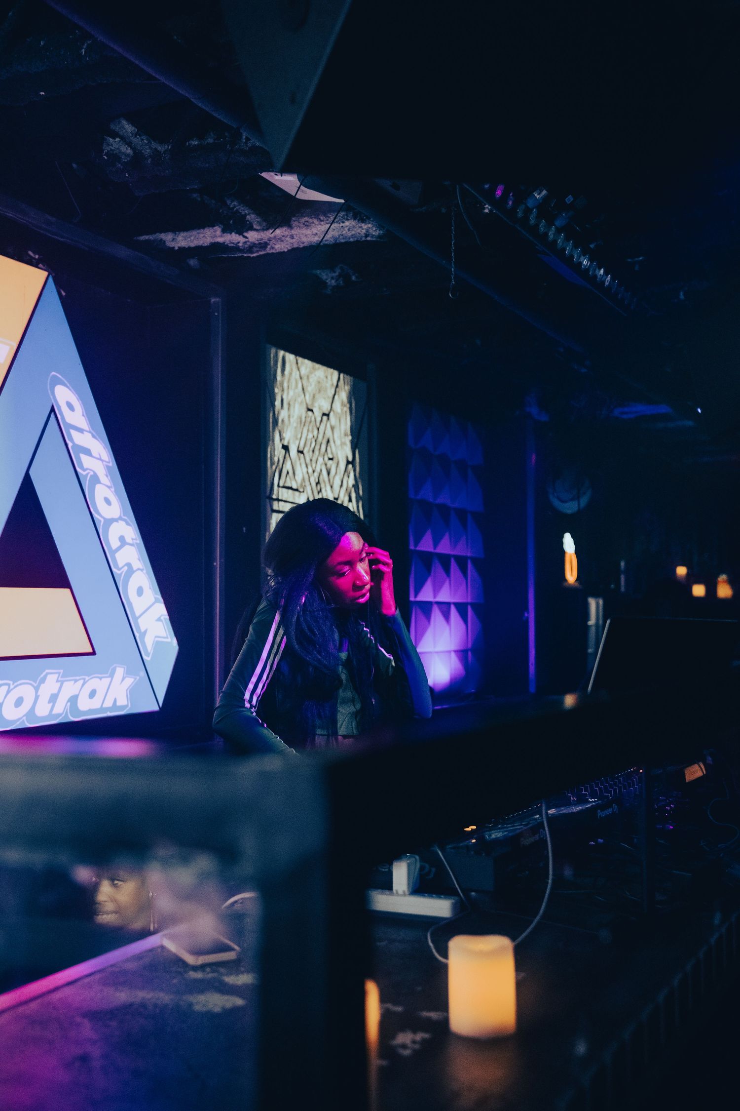 DJ performing in a nightclub with neon triangular lighting and purple ambiance.