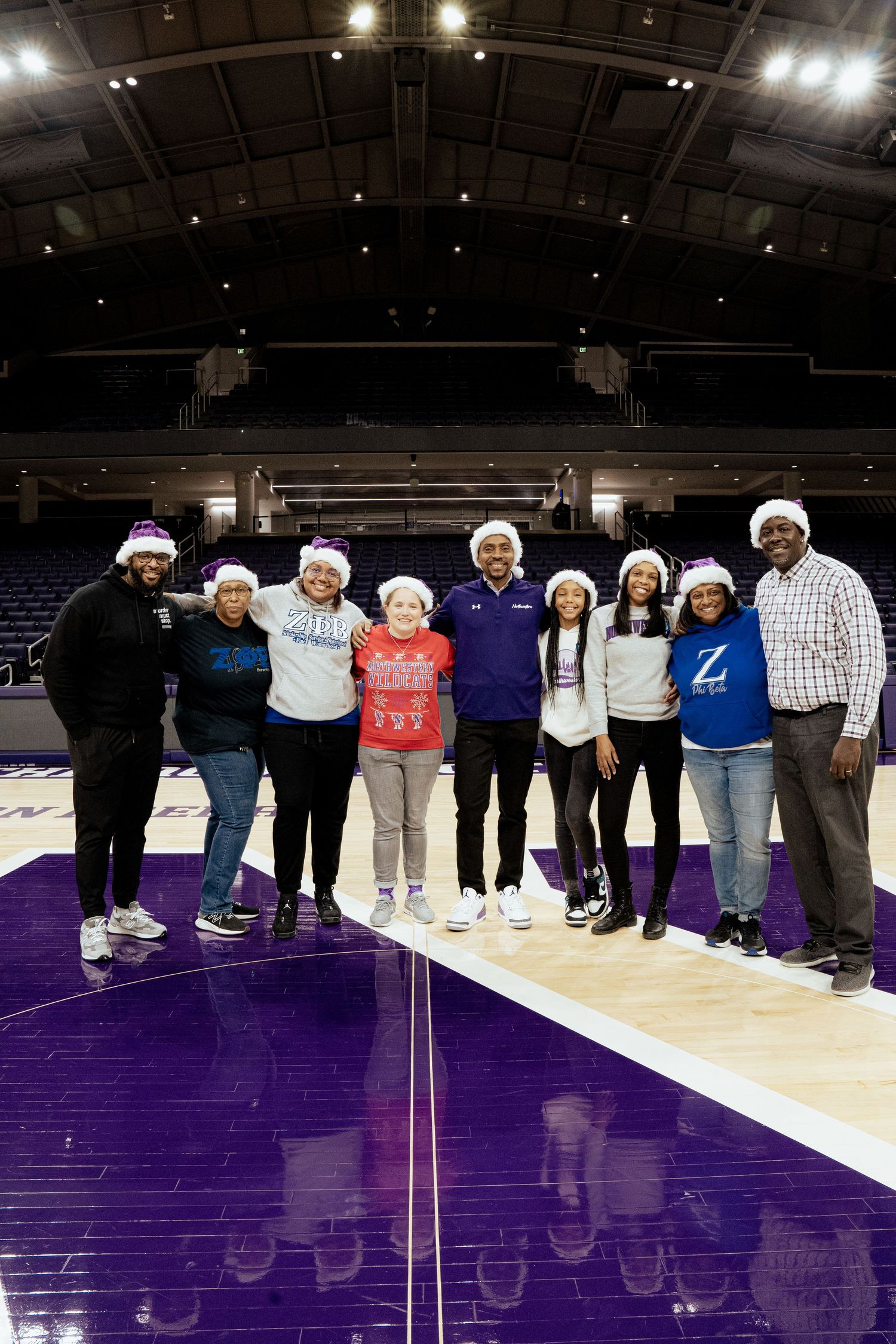Group photo on a purple basketball court wearing winter hats and casual attire.