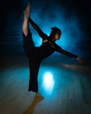 Silhouetted dancer in black performing a dramatic pose against vibrant blue lighting.