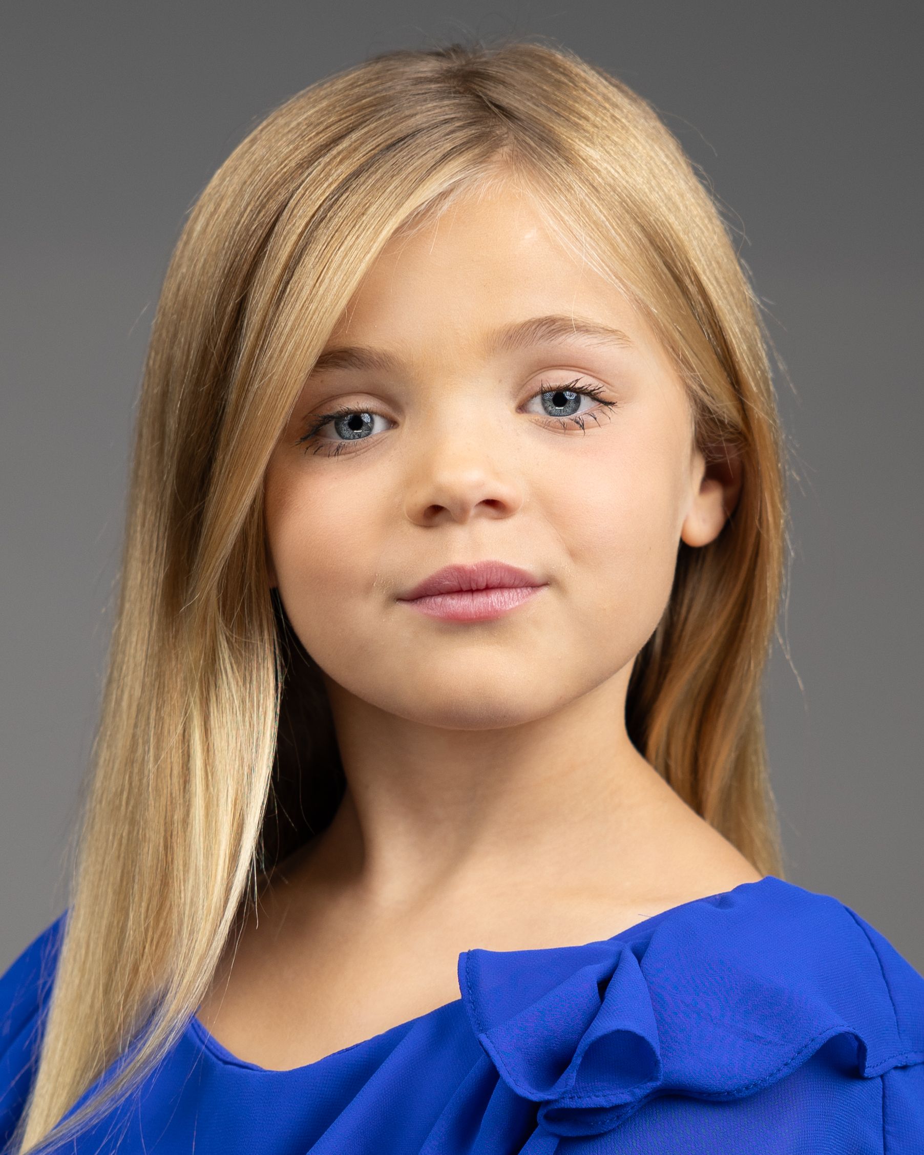 Studio headshot with bright blue ruffled top against neutral background.