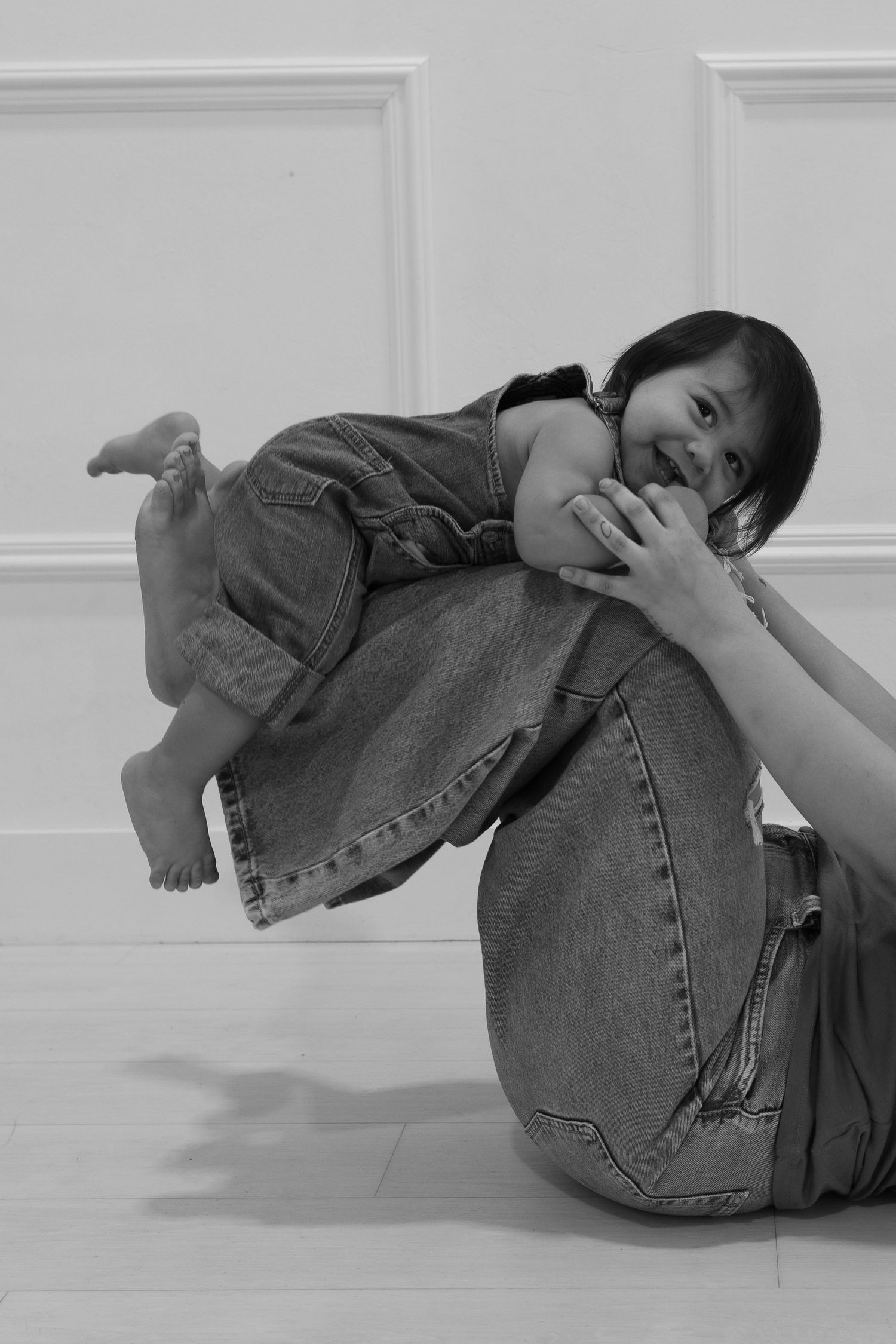 A playful black and white portrait of a parent and child against a white wall.