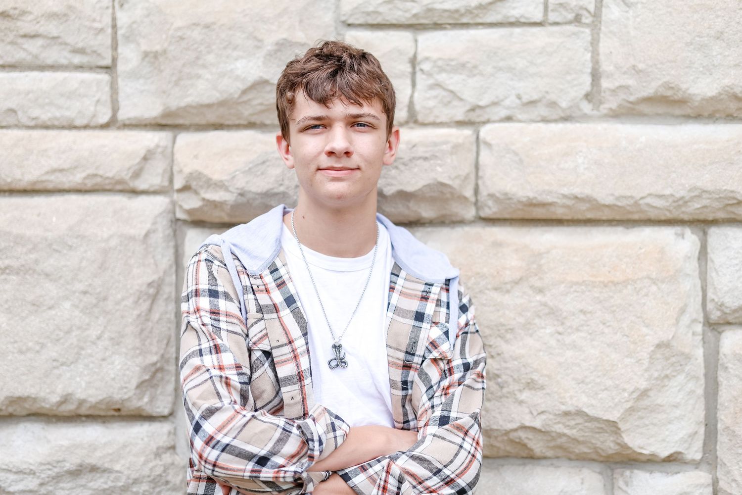 Close up of senior in white shirt and tan plaid jacket leaned again stone building