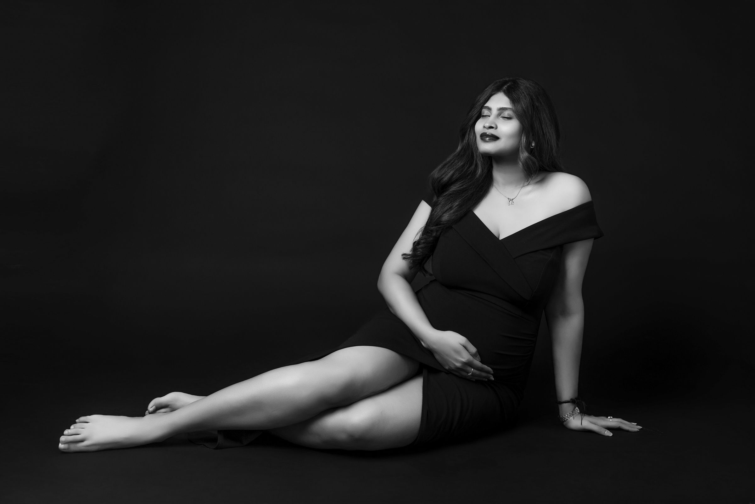 Artistic black and white portrait of a woman in elegant pose against dark backdrop.