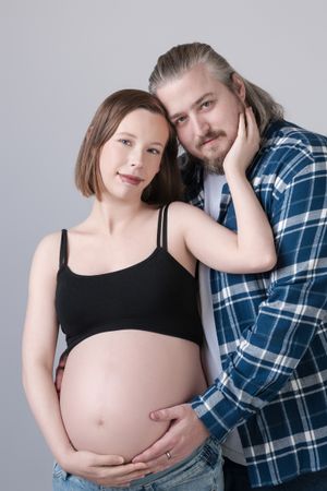 Intimate maternity portrait of couple in studio with woman in black tank top and man in plaid shirt.