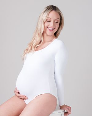 Pregnant woman in white bodysuit poses elegantly on light background.