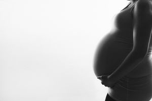 Minimalist black and white silhouette highlighting pregnant belly against white background.