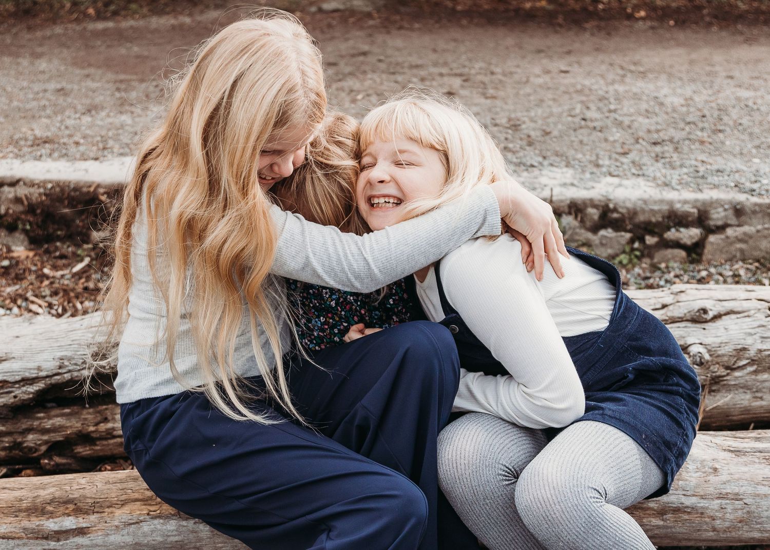 Three sisters sharing a joyful embrace while sitting outdoors.