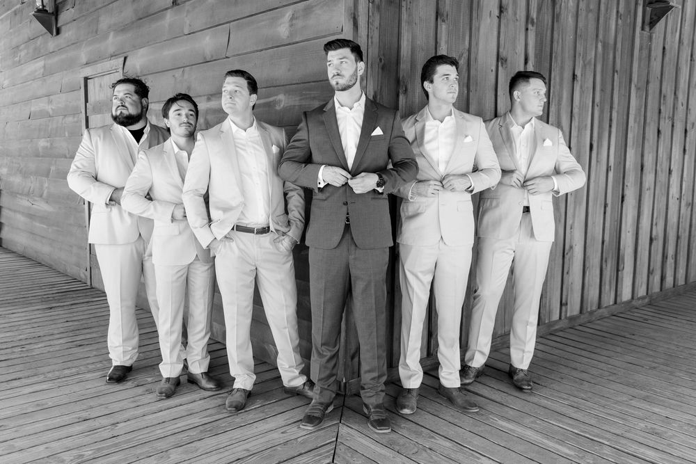 Black and white photo of groomsmen in formal attire posing together on a wooden deck for a wedding portrait.