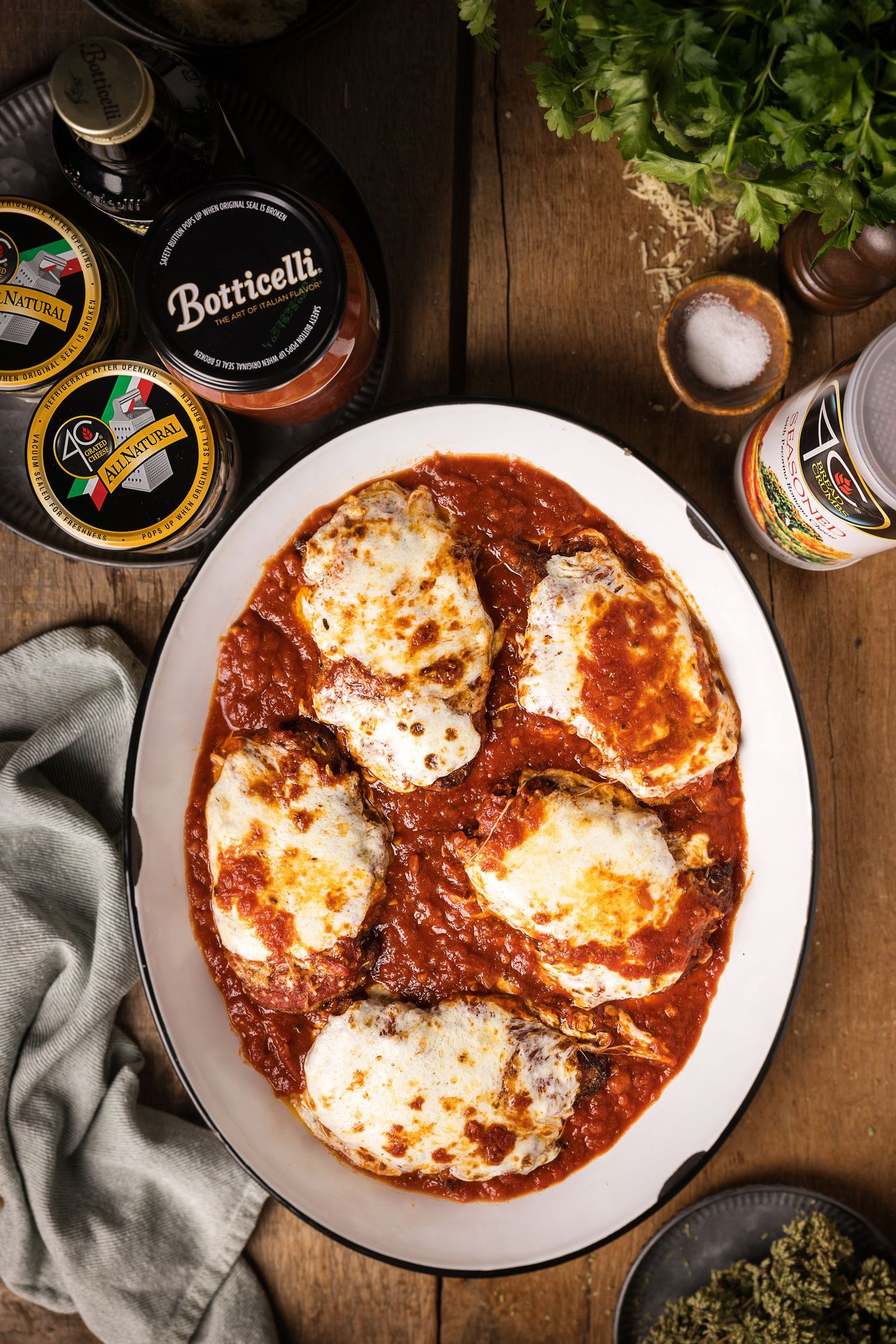 Chicken parmesan in tomato sauce topped with melted mozzarella on a white oval platter with Botticelli sauce nearby.
