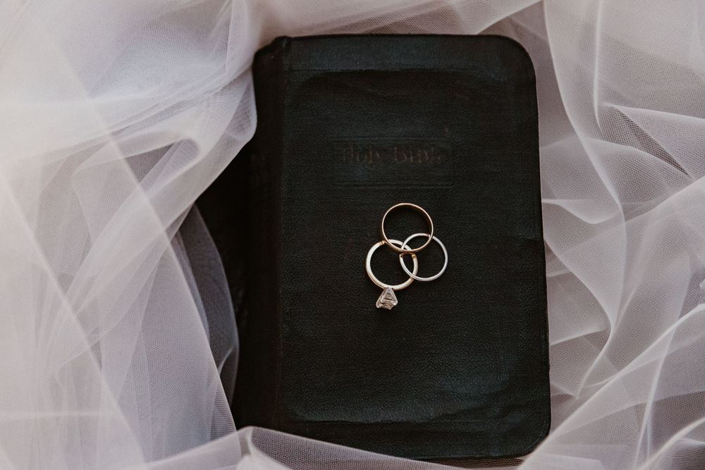 Wedding rings placed on black Bible with delicate white tulle fabric.