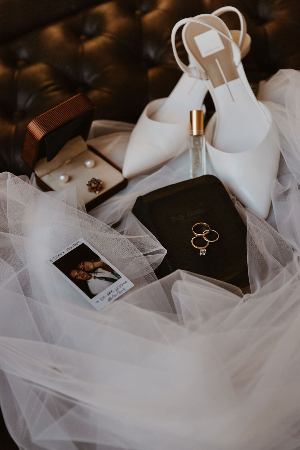 Wedding rings displayed on black Bible surrounded by elegant white tulle fabric.