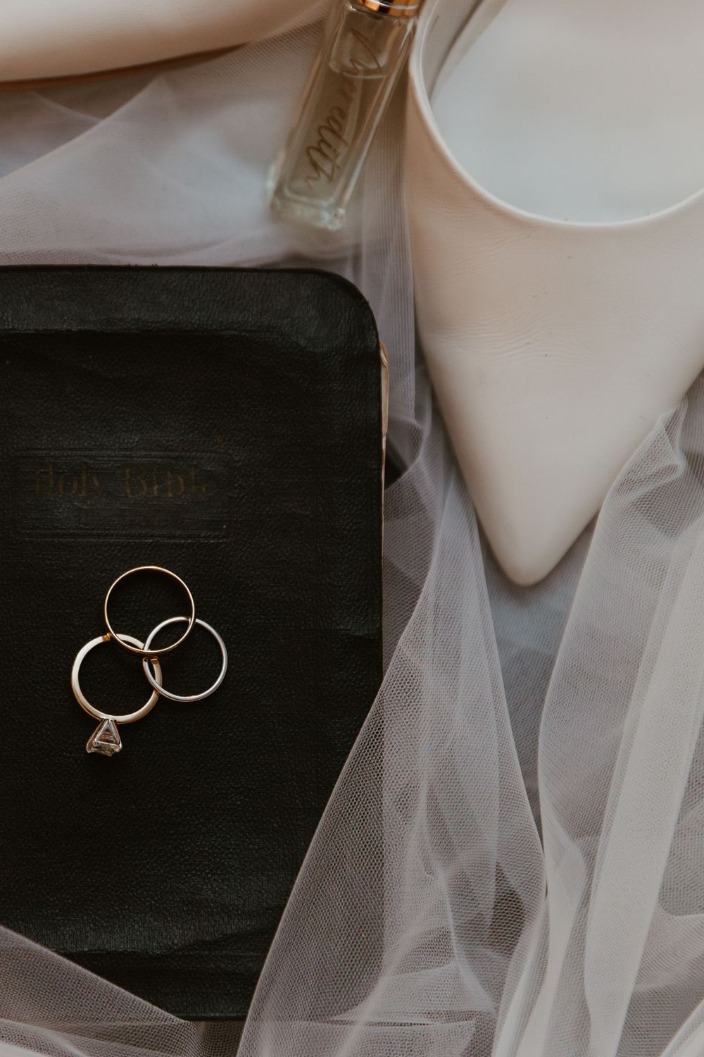 Wedding bands and jewelry arranged artistically on dark surface with white tulle accents.