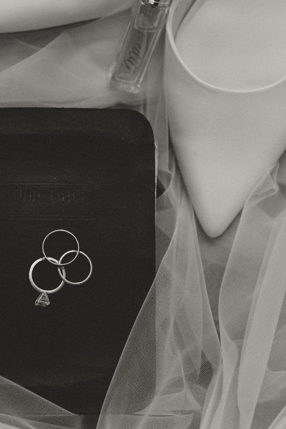 Wedding rings and diamond jewelry photographed on black surface with soft white fabric.