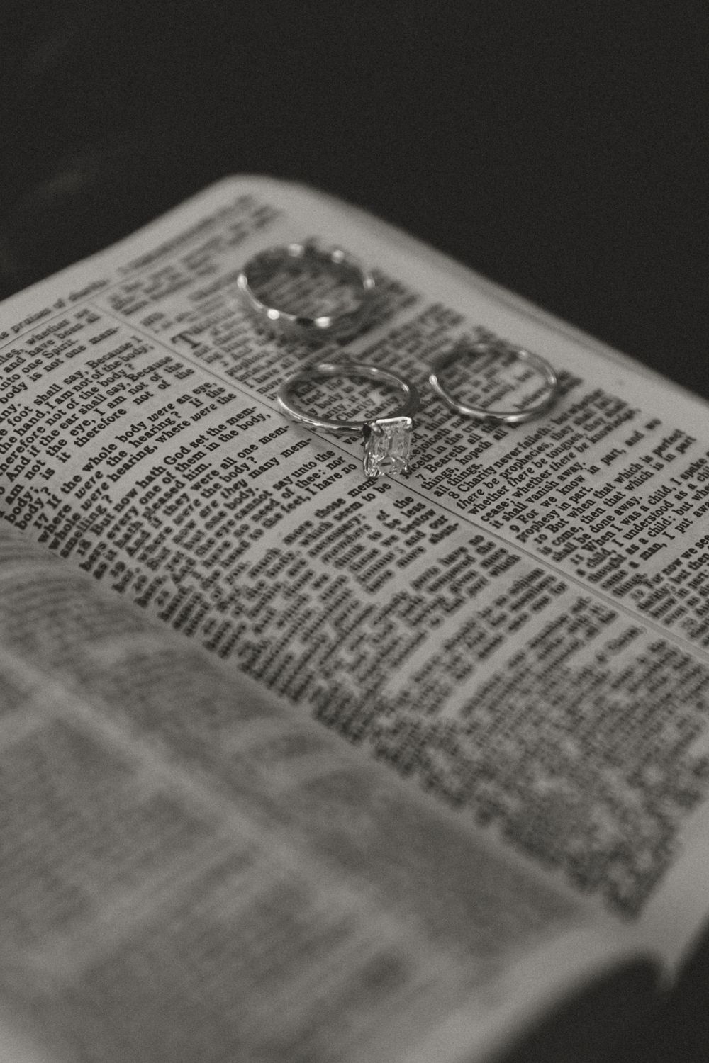 Wedding rings photographed on an open Bible page with dramatic lighting.