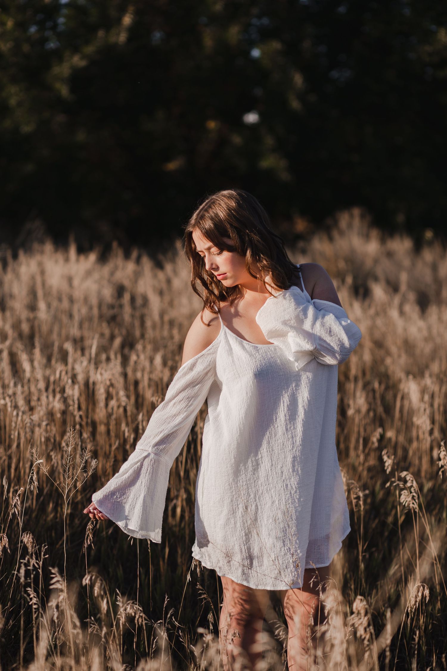 Woman standing in tall grass at sunset with wind-blown hair and a distant gaze | Emotive portrait session in the Tampa Bay area