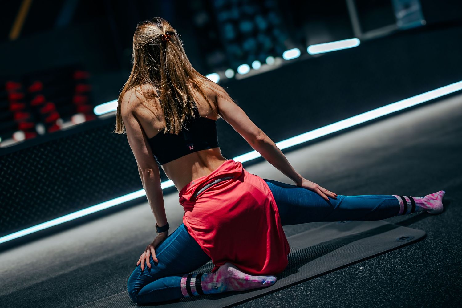 An athletic woman performs a dramatic split pose in a dark gym setting.