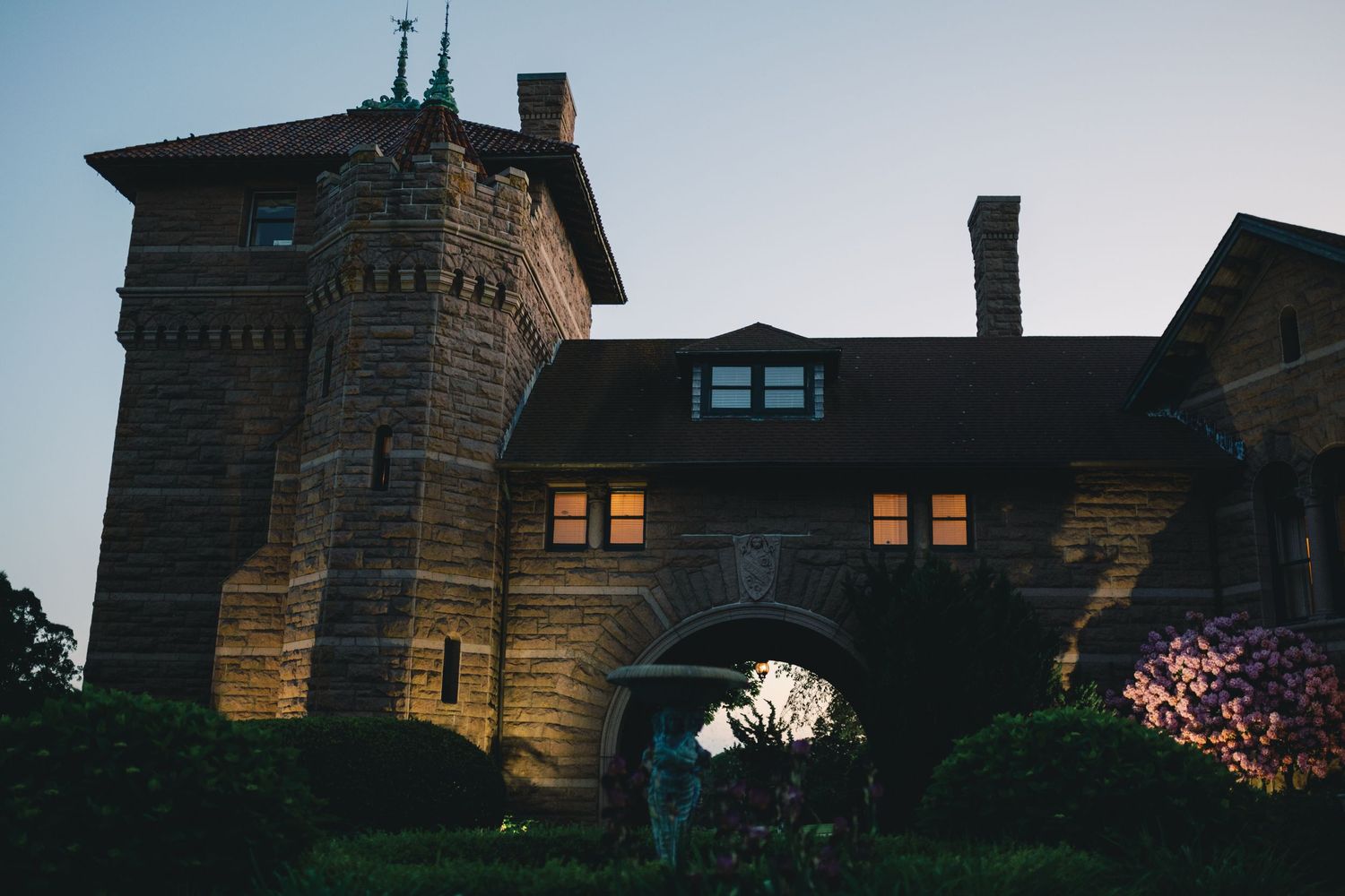 Historic stone mansion illuminated at dusk with glowing windows and ornate architectural details.