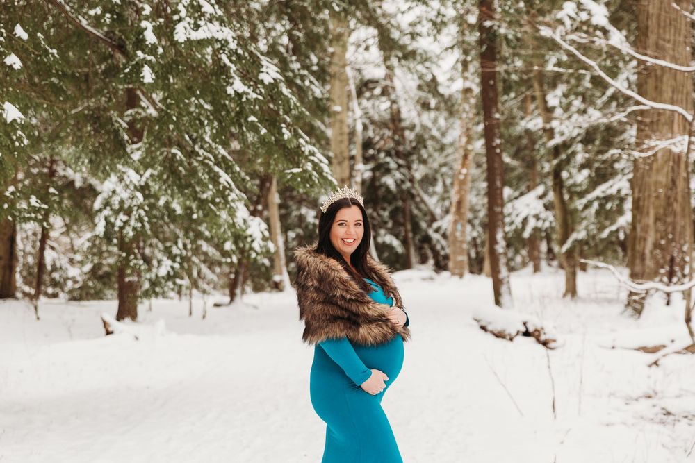 Winter maternity photos captured in a snow-covered forest with evergreen trees in the background.