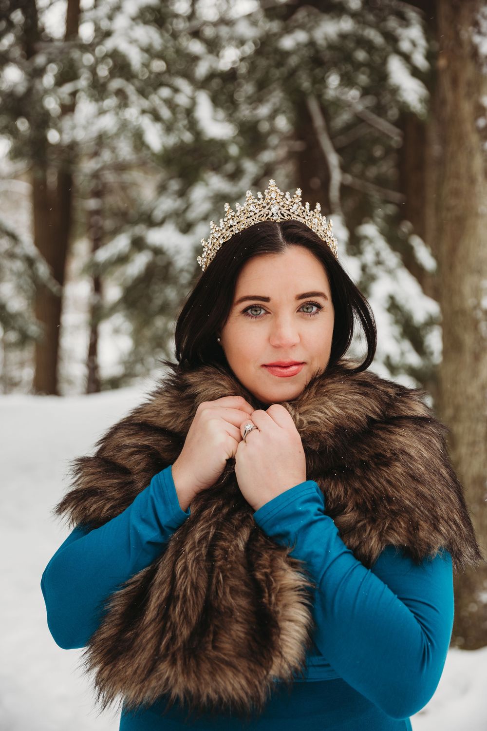 A winter maternity portrait featuring a fur-trimmed wrap and delicate crown in a snowy forest setting.