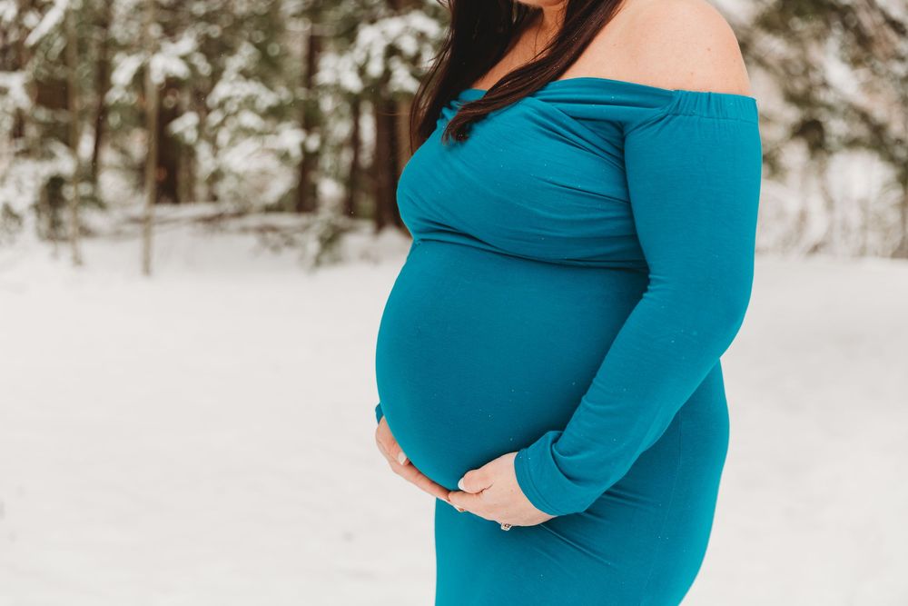 A winter maternity session showcasing an elegant teal gown against fresh white snow.