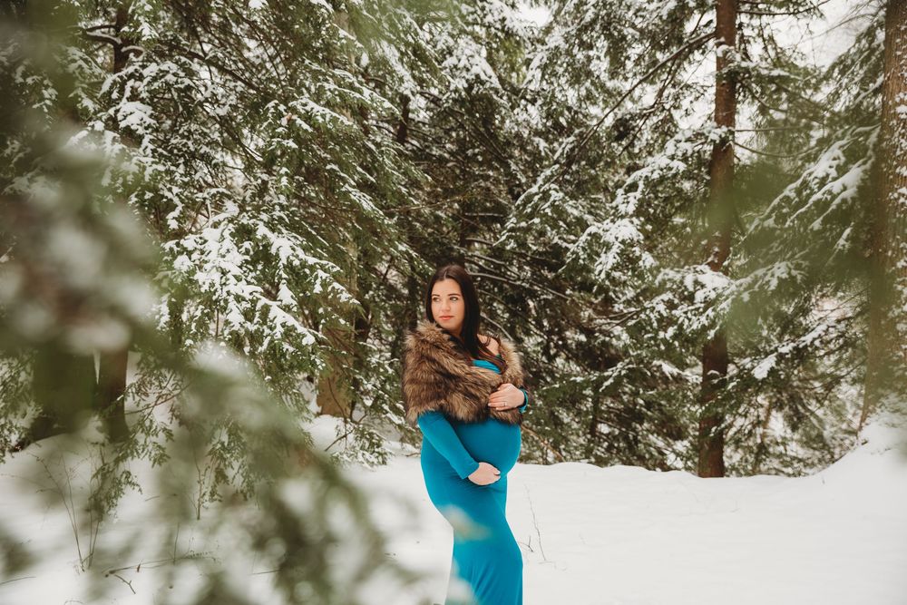 Artistic maternity photograph featuring a bright blue gown in a wintry forest setting.