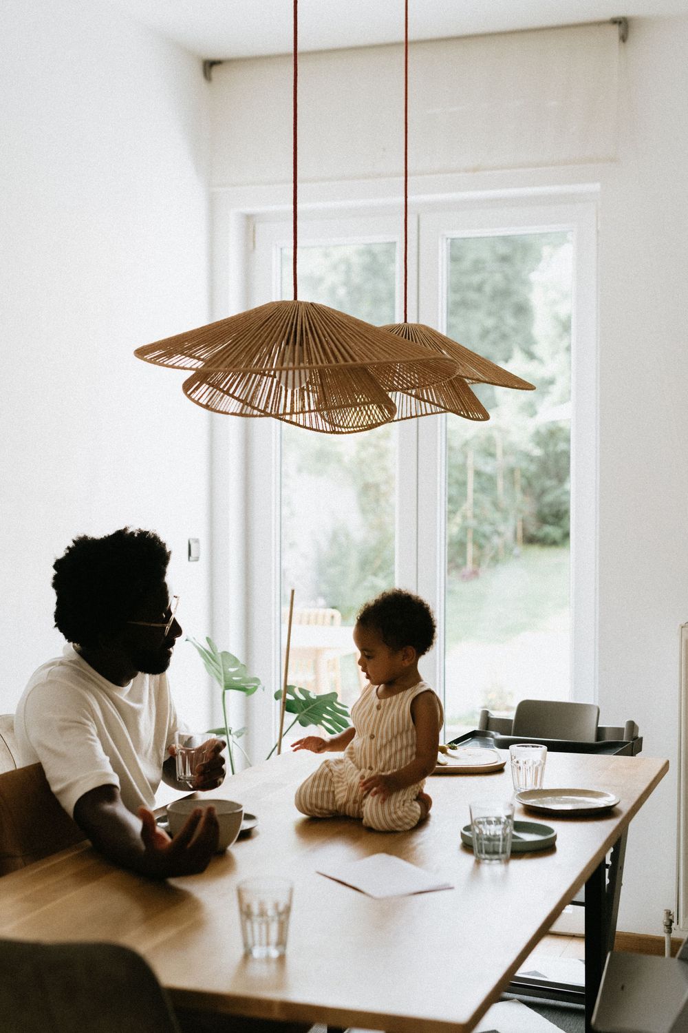 Minimalist dining room features rattan pendant lights and natural light from large windows, creating a serene atmosphere.