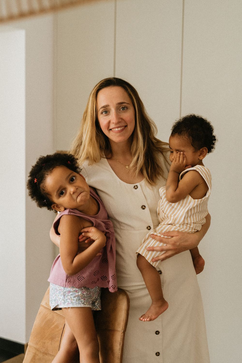 A loving family moment captured indoors with a parent and two children in casual attire against a white wall.