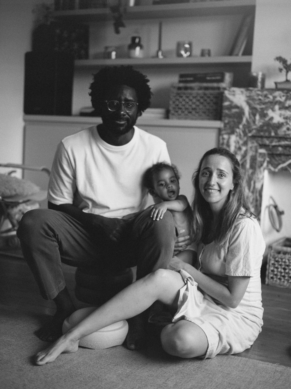Black and white image showing figures sitting together on floor in cozy indoor setting creating intimate candid moments.