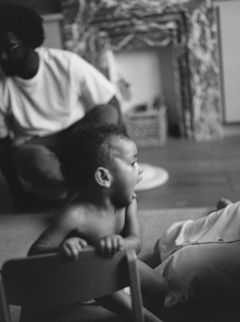 A black and white candid portrait of a small child leaning on a cushion in a contemplative pose.