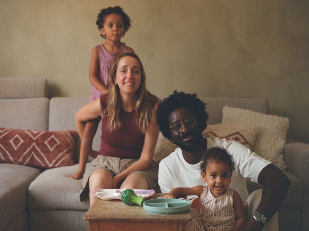 Happy family sitting together on grey couch at home, spending quality time reading with their children.