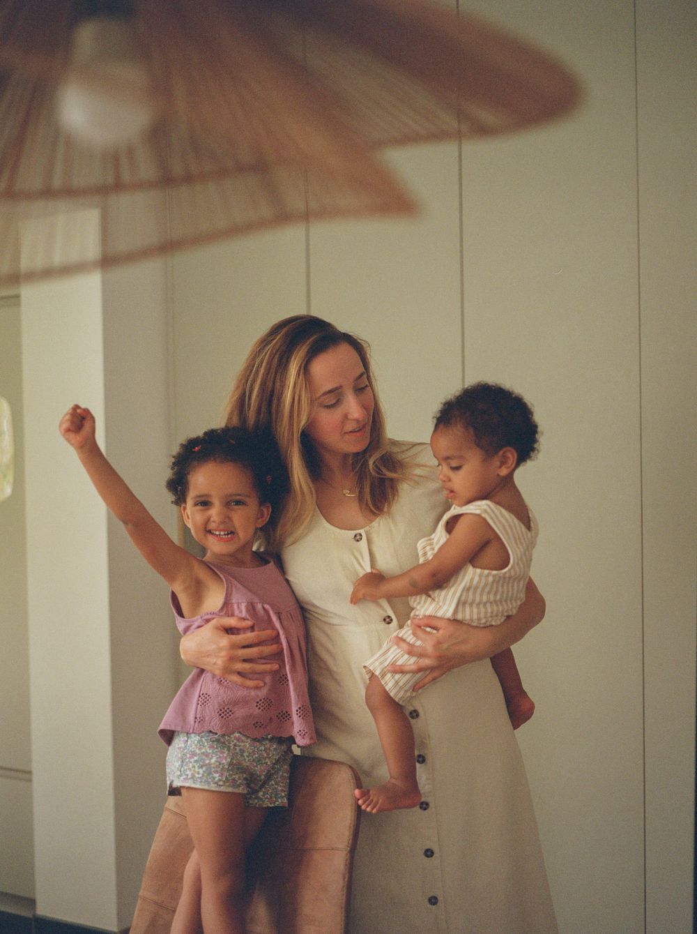 A warm family moment captured indoors with a parent and two children in natural lighting.
