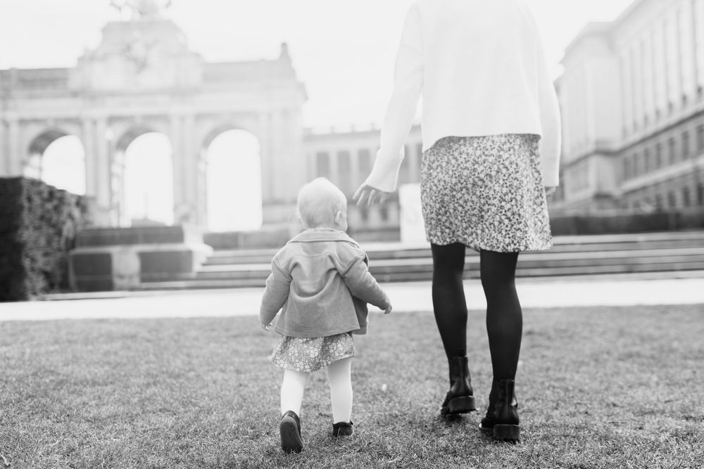 Black and white photo of toddler walking with adult near historic building.