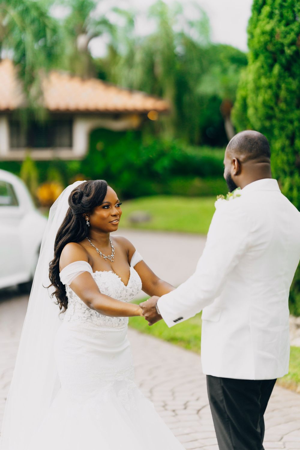 A couple shares a romantic moment on their wedding day in a lush garden setting wearing white attire.