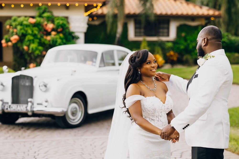 A happy couple shares a romantic moment in front of a classic white Rolls Royce during their outdoor wedding ceremony.