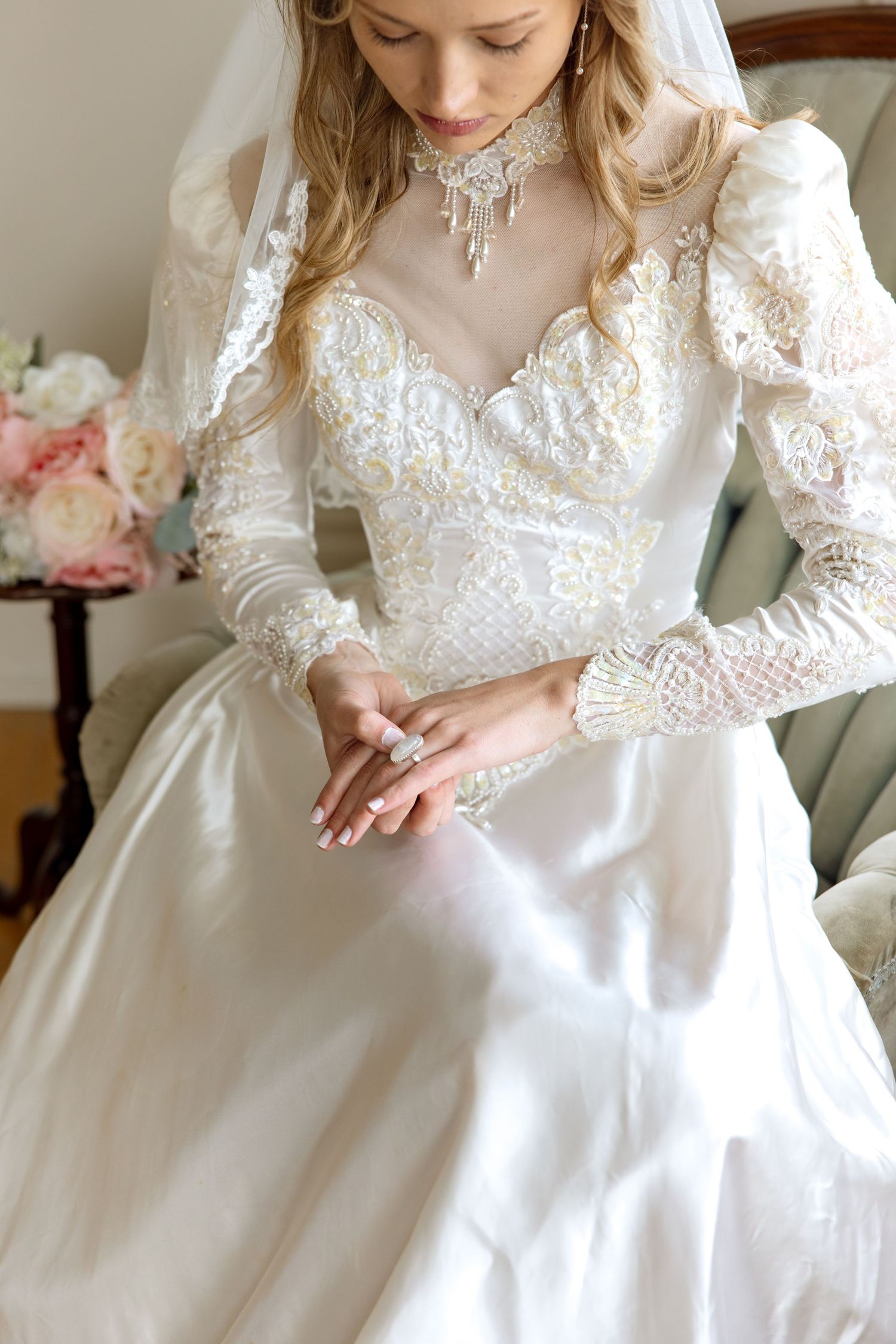 Elegant vintage-style wedding dress with long lace sleeves, high neck, and intricate beaded details shown in close-up view.