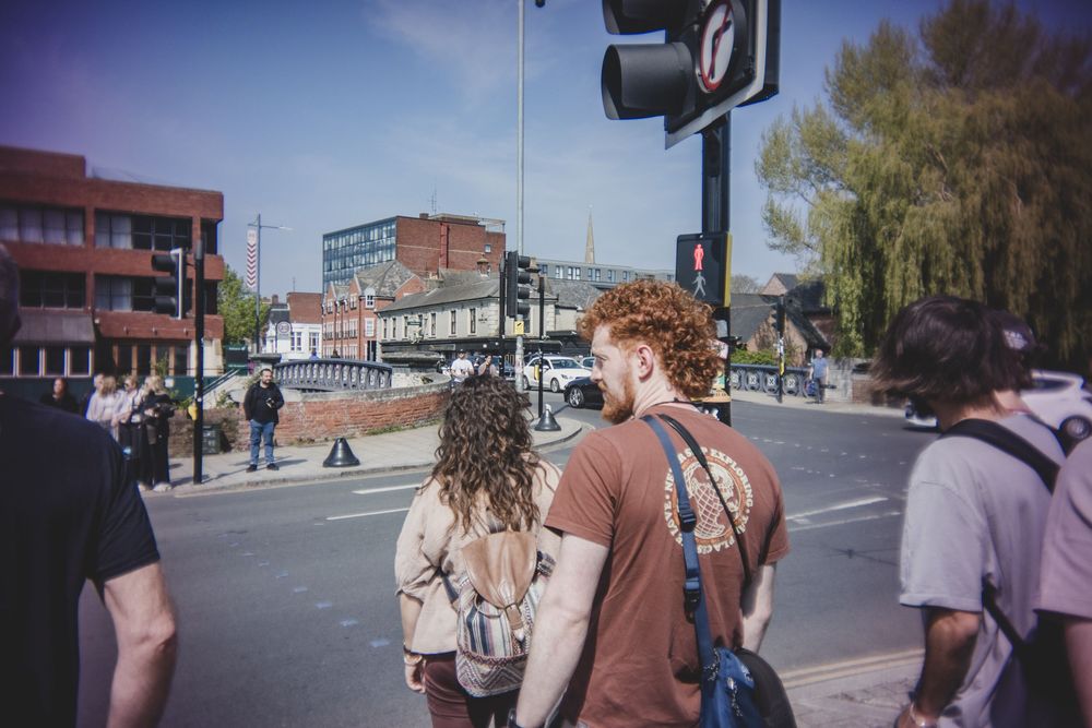 People waiting to cross a city street intersection on a sunny day in an urban neighborhood.