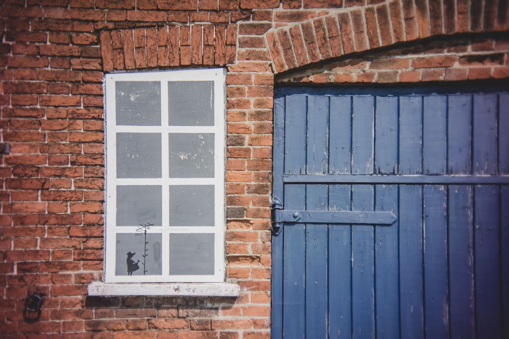 Red brick wall exterior with white framed window and blue wooden door showing classic architectural details.