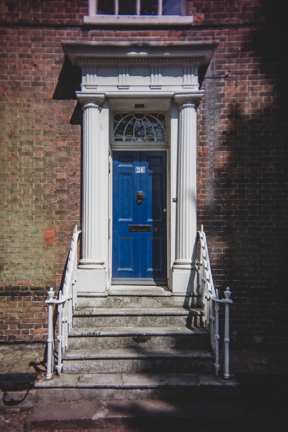 A bright blue door with classical white columns and a fanlight sits atop brick steps with white metal railings.