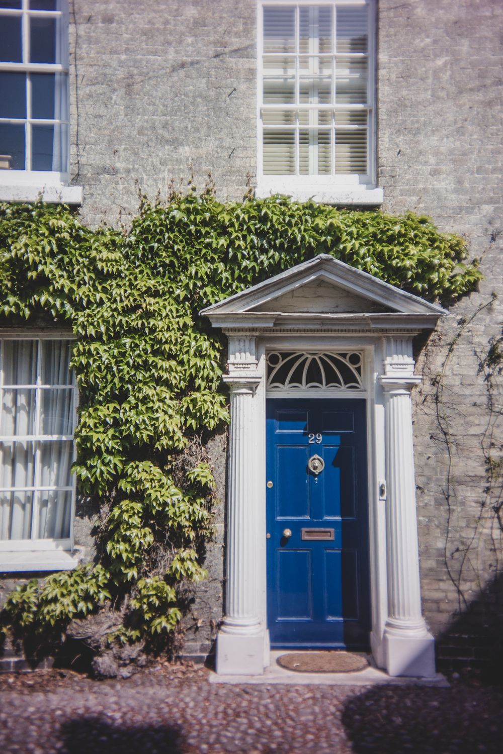 Elegant blue Georgian door with white columns and a vaulted archway set against an ivy-covered stone facade.