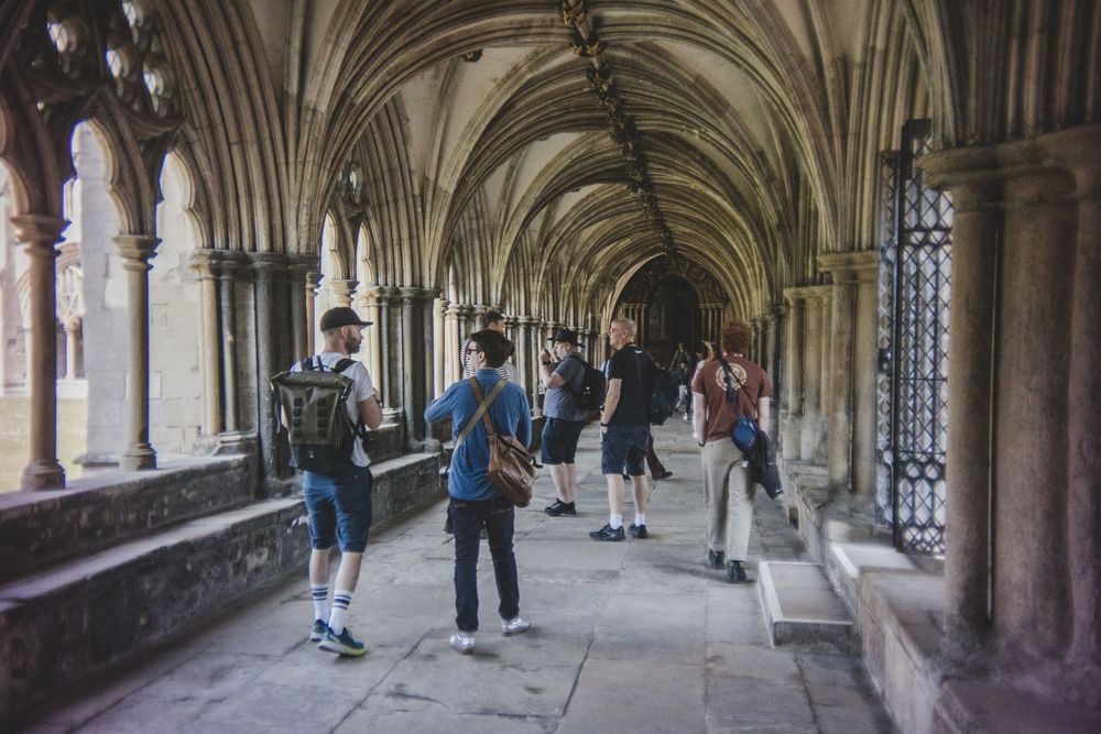 Tourists walk through a gothic arched corridor with vaulted ceilings in Westminster Abbey's historic cloisters.
