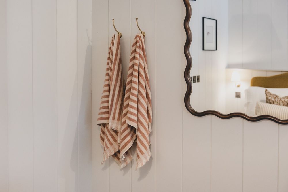 Two striped brown and white towels hanging on hooks against a white shiplap wall beside a decorative mirror.