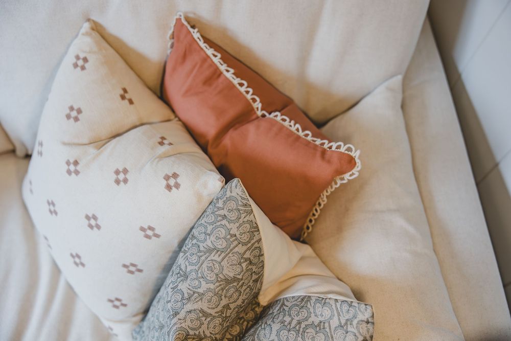 Decorative throw pillows in neutral tones with floral and geometric patterns arranged on a cream sofa.
