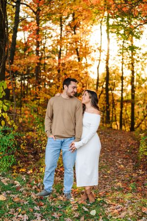 A couple shares a romantic moment on a forest trail surrounded by vibrant autumn foliage and golden sunlight.