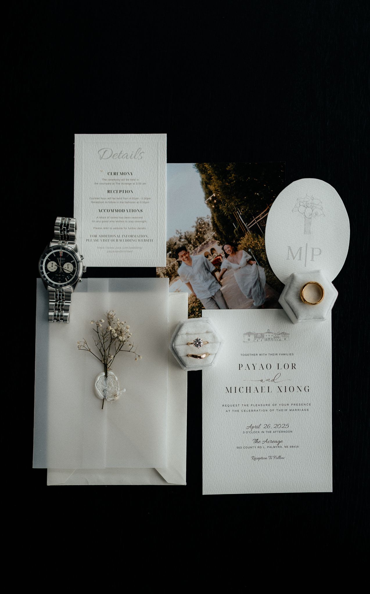 Wedding invitation suite with elegant stationery, watch, and dried flowers on dark background.