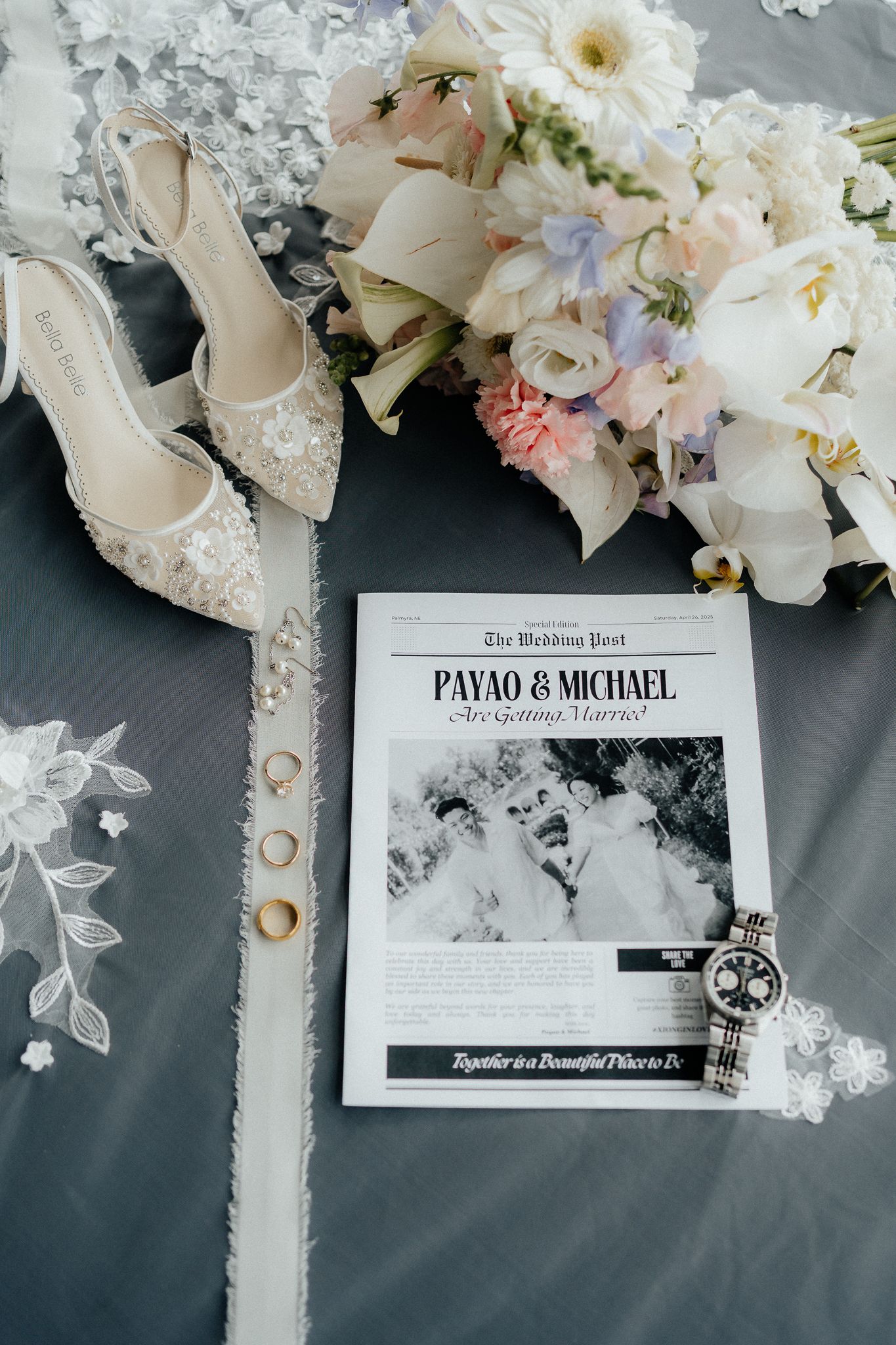 Wedding day details with lace heels, rings, bridal bouquet of white flowers, and black and white newspaper announcement.