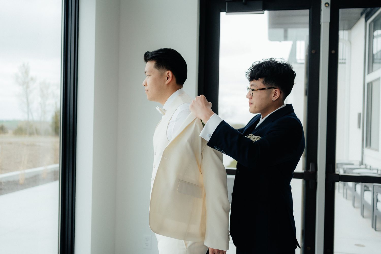 Best man helps groom prepare by adjusting his white jacket before the ceremony.
