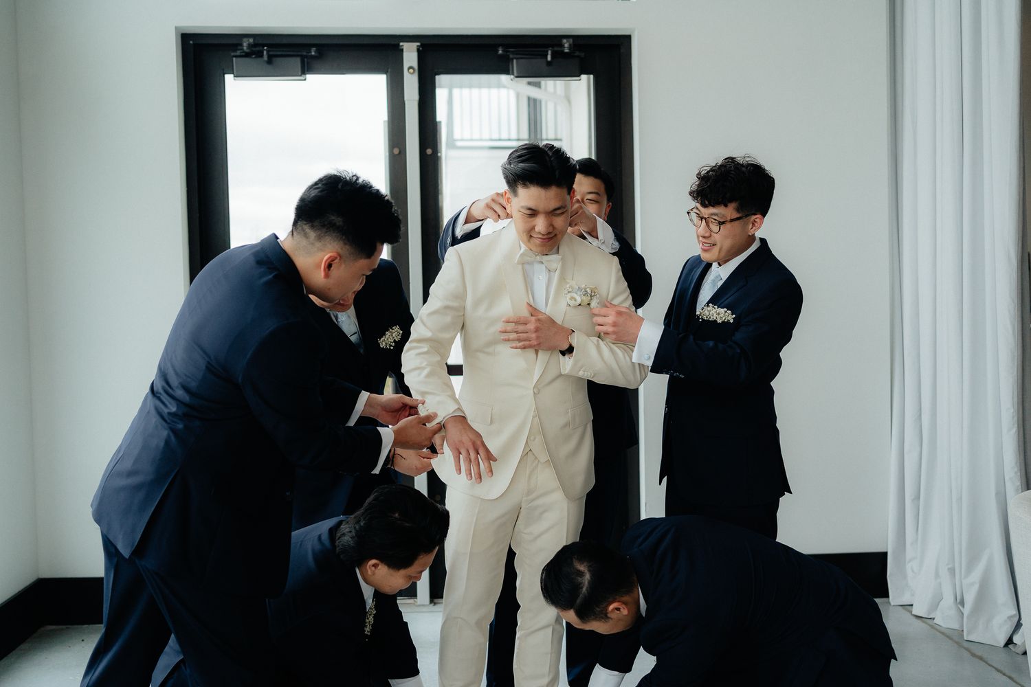 Wedding party helping the groom get ready in a bright indoor setting.