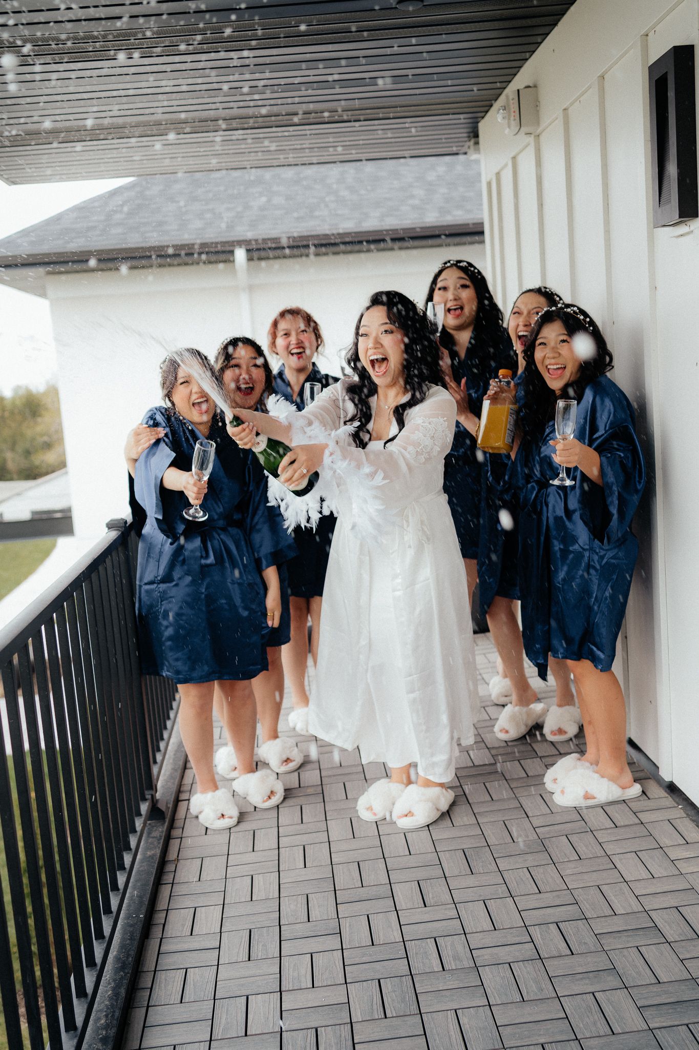 A bridal party wearing casual denim jackets celebrates joyfully on a balcony with confetti flying in the air.