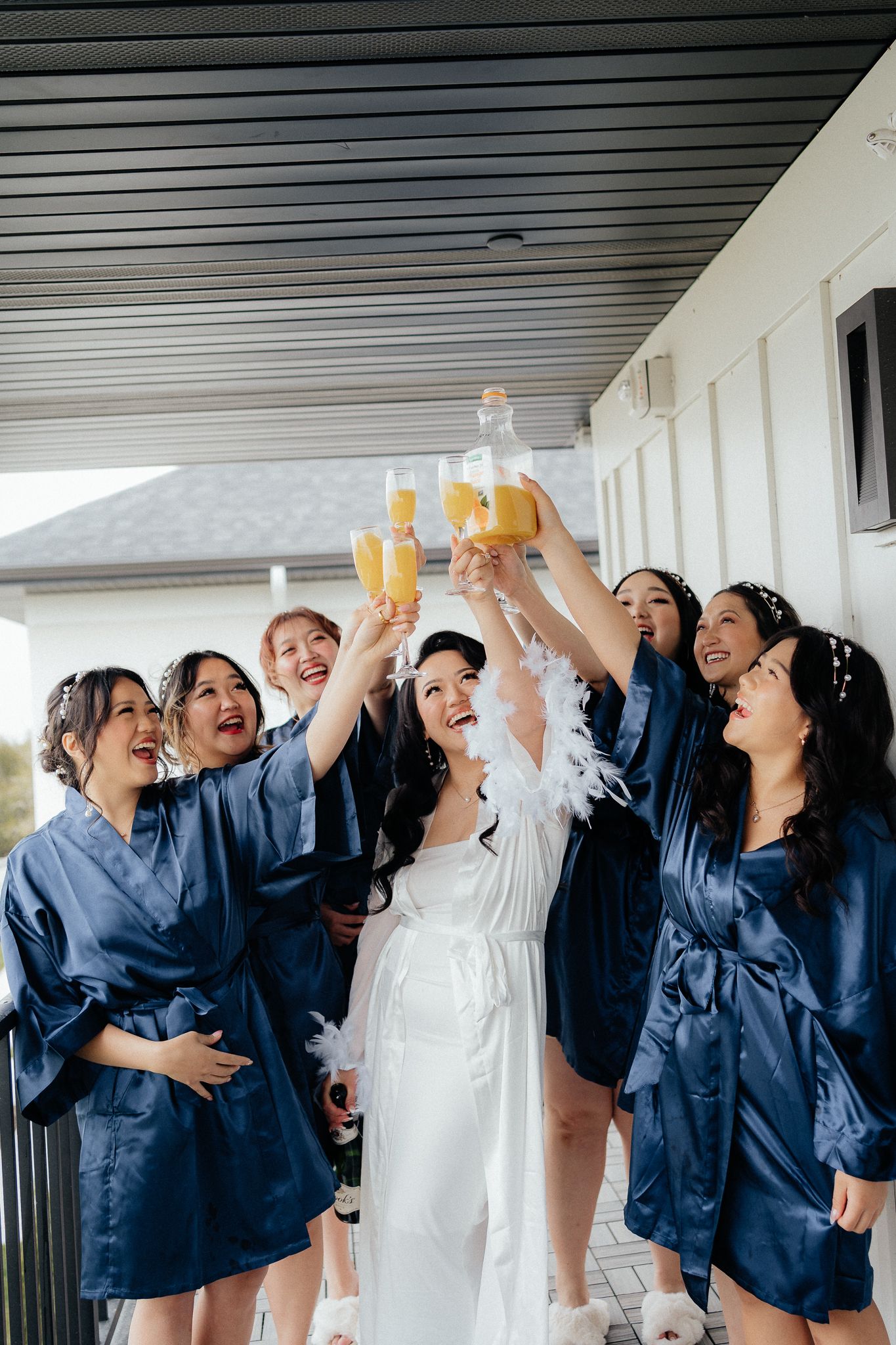 Bride and bridesmaids in navy robes toasting with champagne on a porch.