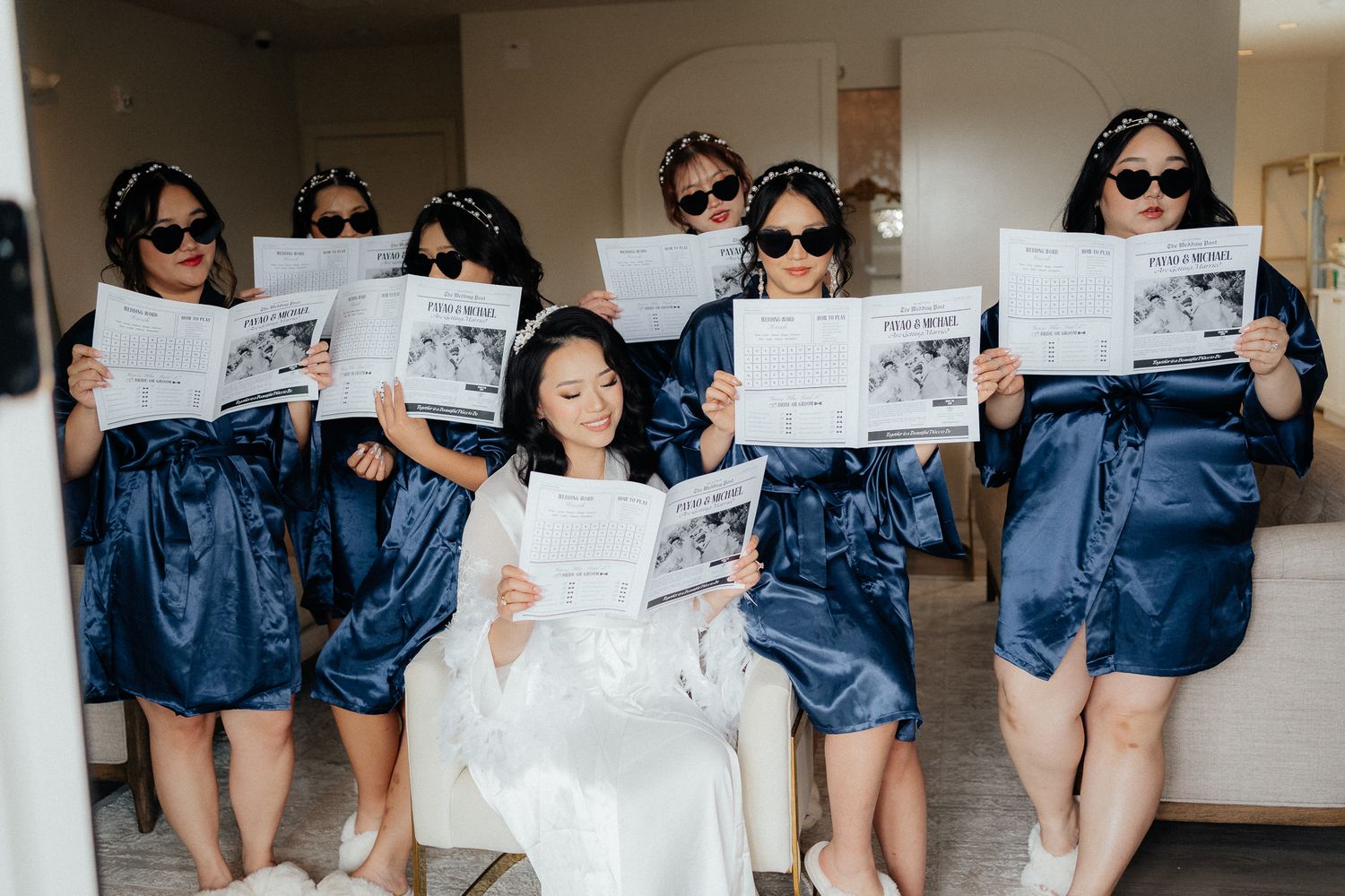 Bridesmaids in matching denim outfits and sunglasses hold up newspapers during a fun wedding photo shoot.